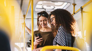 Two females on a bus looking on a phone. 