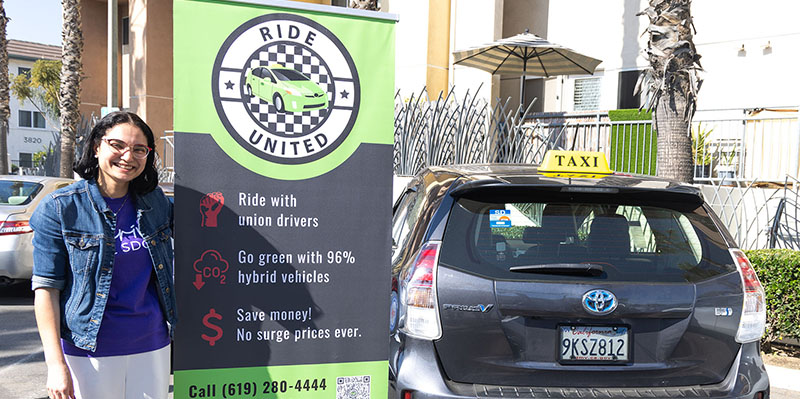 Student standing by taxi poster and taxi car
